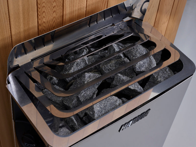 Silver sauna heating unit with gray rocks and brown wood background