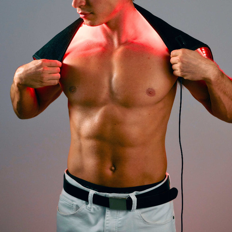 Man using a red light therapy device on his chest against a gray background