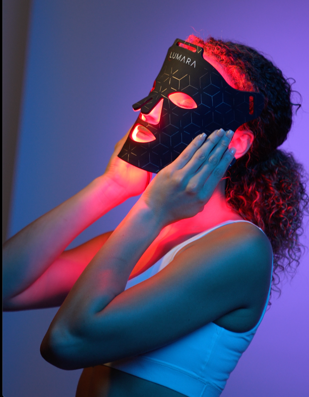 Person wearing a LED face mask with glowing red lights, set against a blue gradient background.